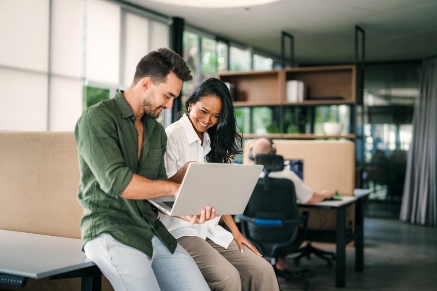 Two coworkers consult a laptop in an office
