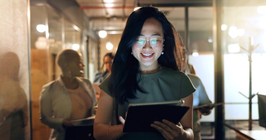 A woman in an office smiles down at a tablet, looking at business data