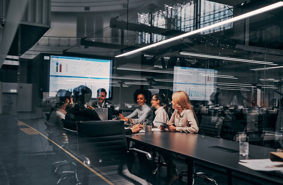 Several people in a glass boardroom speaking around a large rectangular table