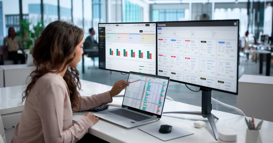 A woman looking at data on a laptop and computer screens in an office