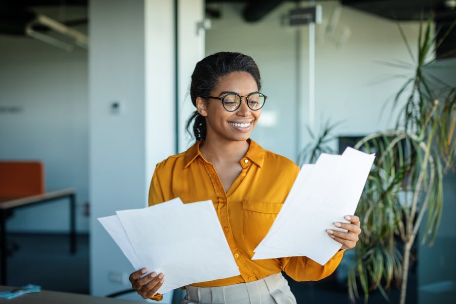 A woman holding two sets of documents in an office and smiling