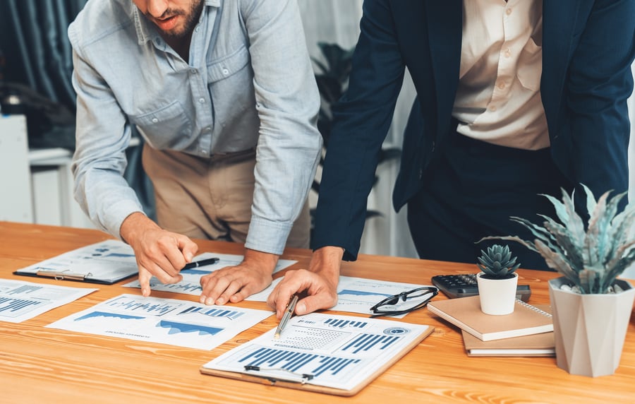 Two colleagues going over paperwork featuring graphs and charts at a boardroom table