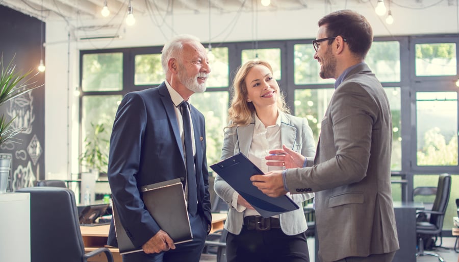 A group of three businesspeople smiling during a conversation in a sunny office