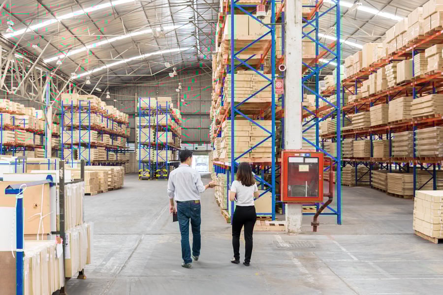 A man and woman walking through a warehouse, both wearing jeans and polo shirts