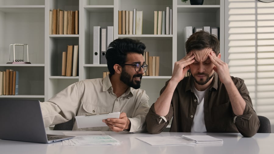 Two coworkers in an office looking at a laptop and seeming very stressed about how much late payments are costing their business