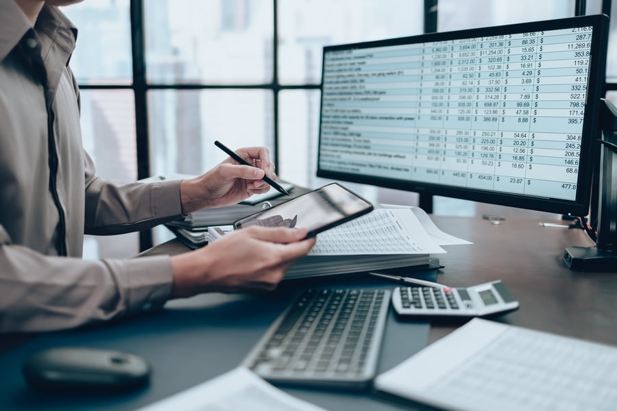 An employee in an office checking numbers on a calculator and spreadsheet