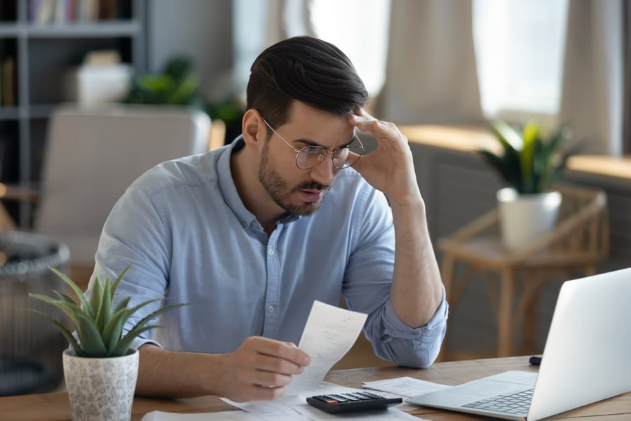 A man looking frustratedly at a laptop in an office setting