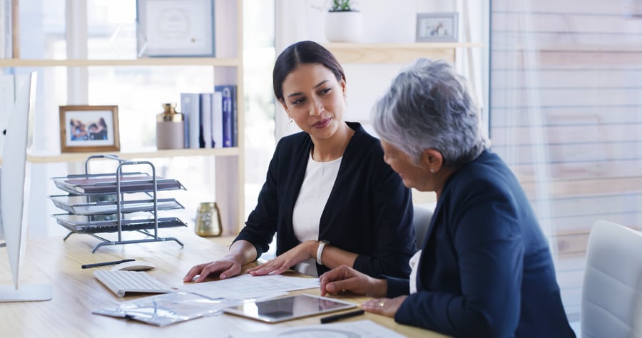 An older and younger woman speak about payment data in an office