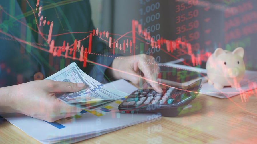 A graphic of a declining red graph overlaid on someone holding cash and typing on a calculator