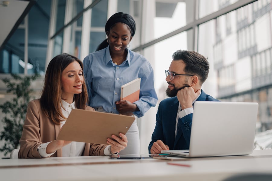 Three people in an office looking at a file and smiling