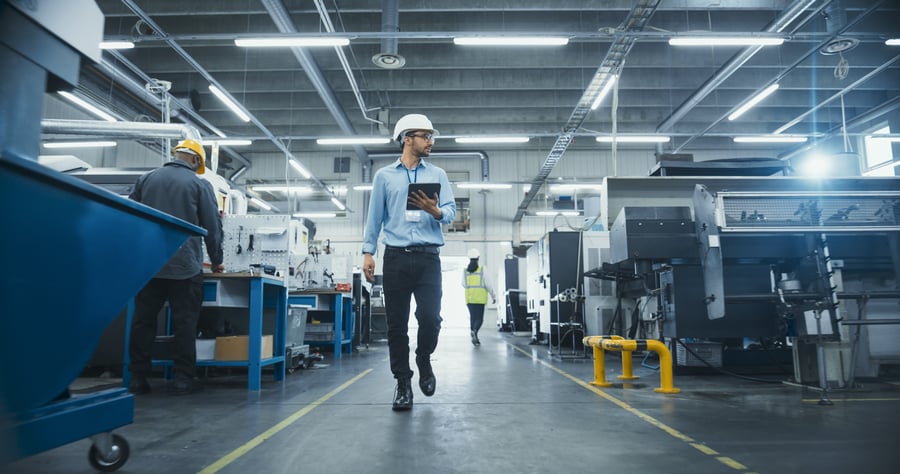 A man holding a clipboard walks through a modern factory