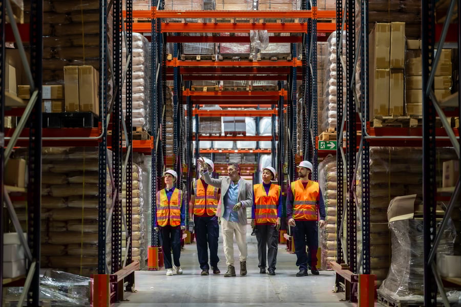 Five people (four in hi-vis, one in business casual) walk through a warehouse