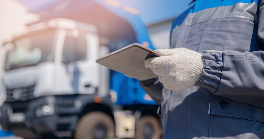 A person in white gloves looking at something on a tablet in front of a transport truck