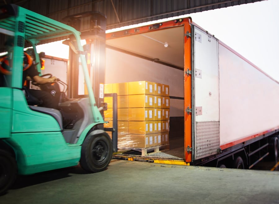 A green forklift loading a white transport truck