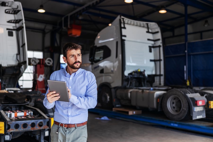 A man with a clipboard assessing two transport trucks in a garage