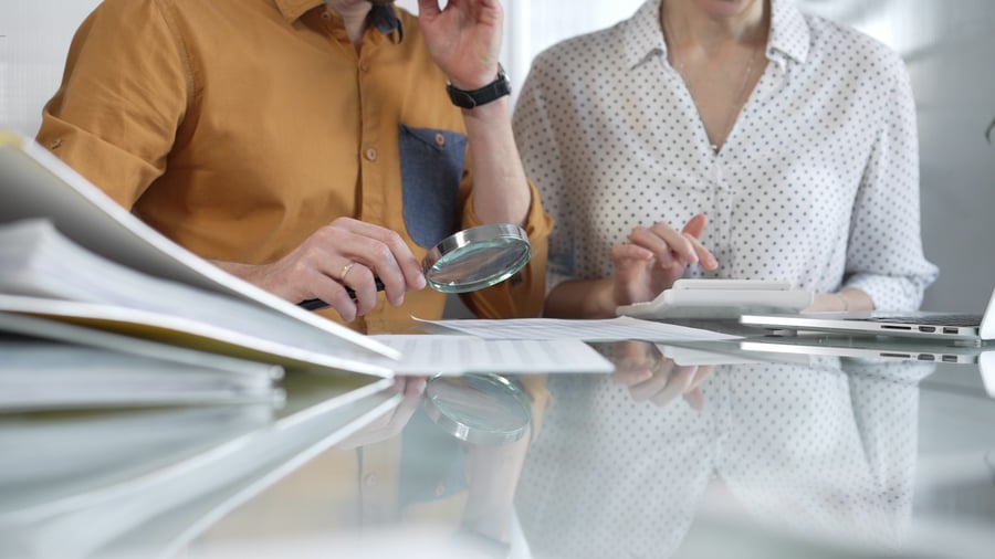 Two people looking at files for b2b fraud prevention with a magnifying glass
