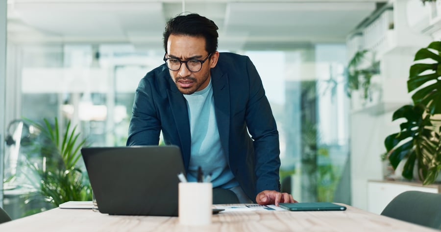 A man looking concerned at something on his laptop in an office