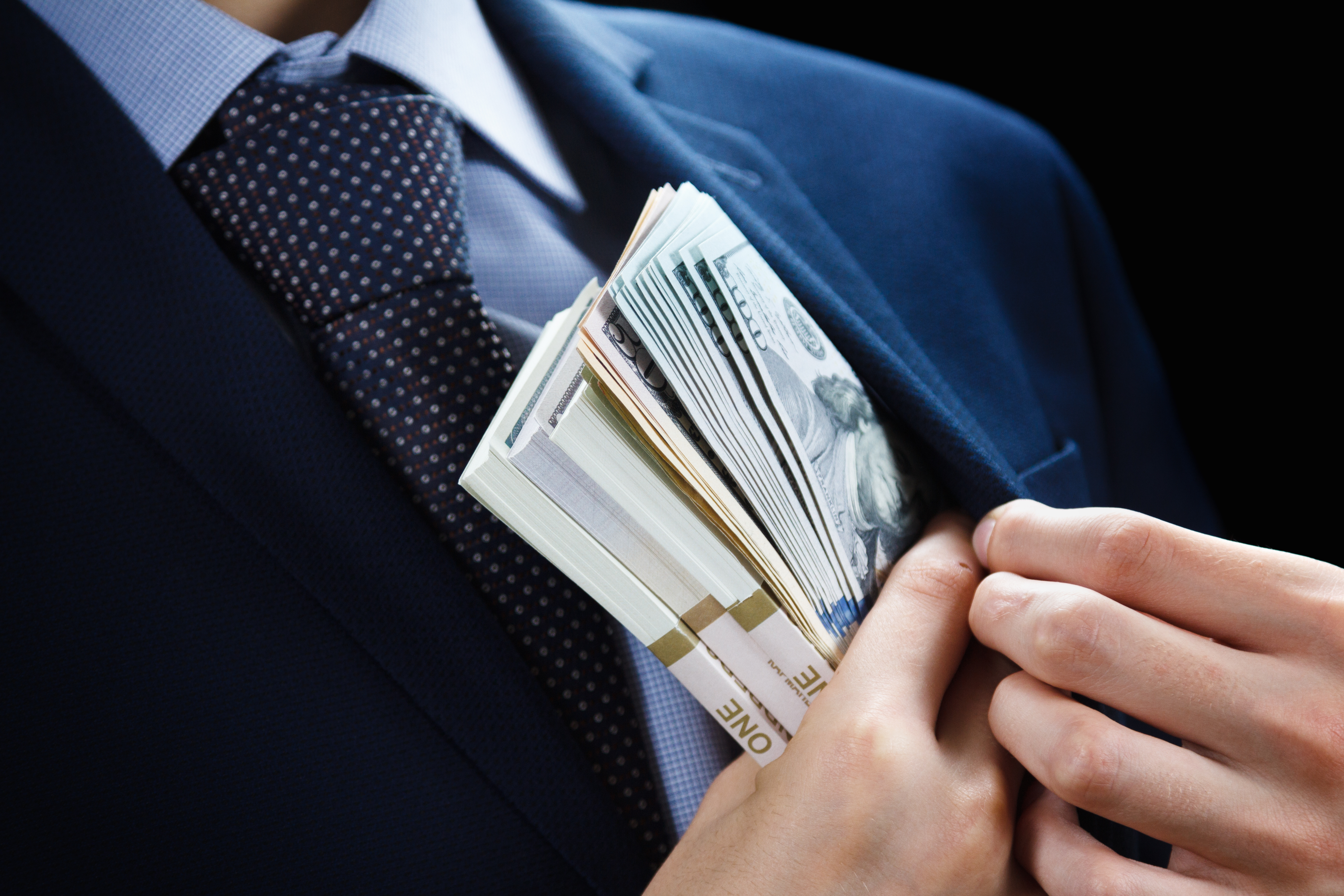 A man stuffing cash into his suit jacket