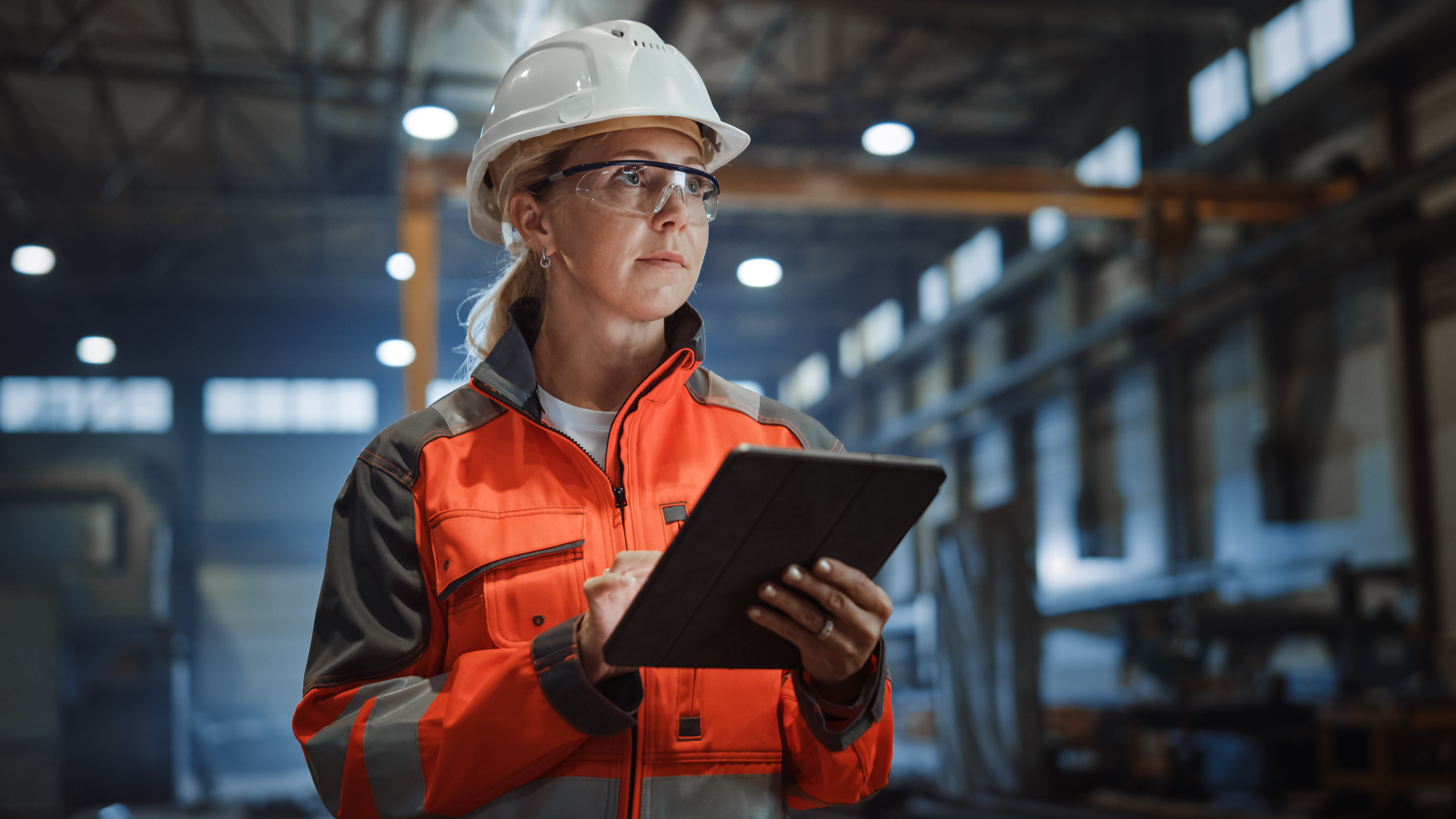 A woman in a hardhat taps something on a tablet in a warehouse