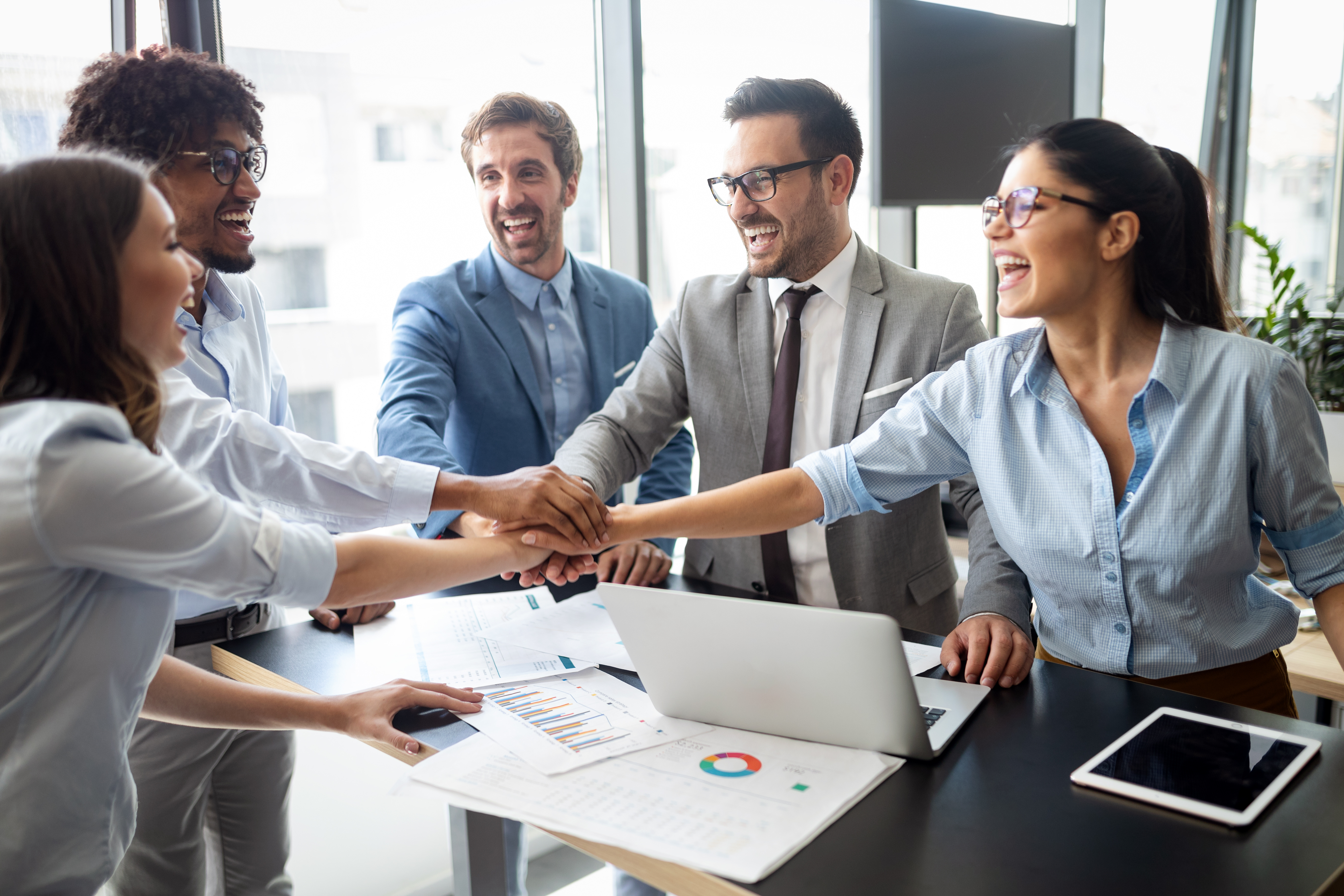 A team putting their hands in the middle of a boardroom table in celebration
