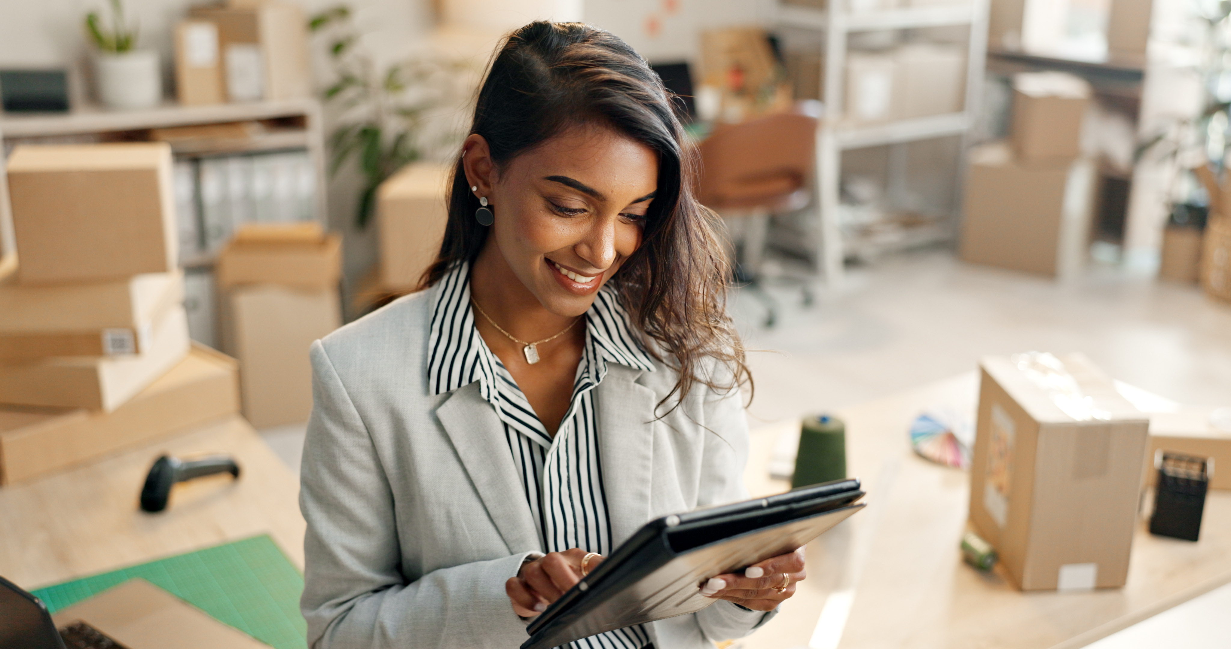 A woman smiling down at a tablet surrounded by boxes