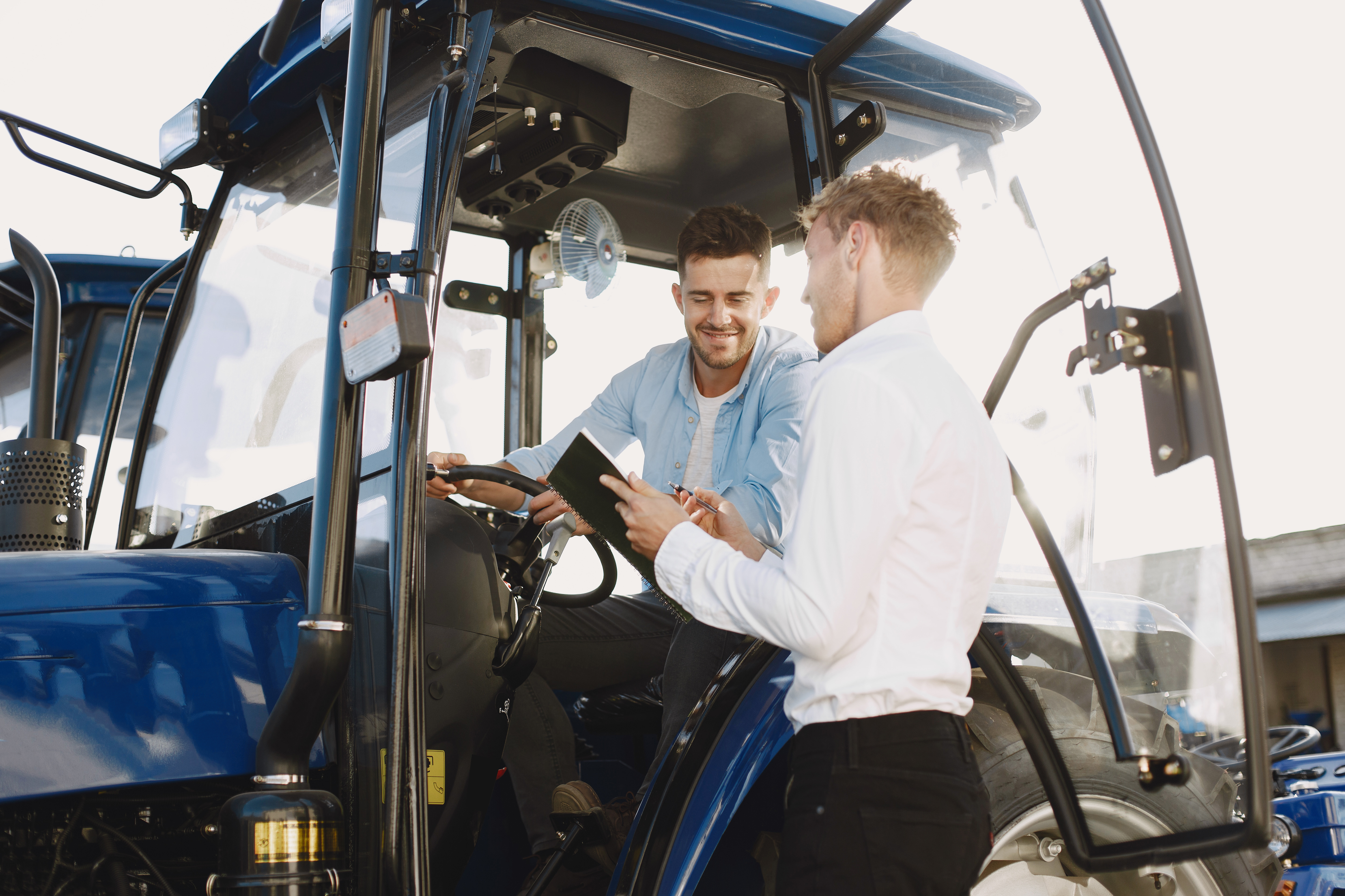 Two men speaking, one sitting in a blue tractor