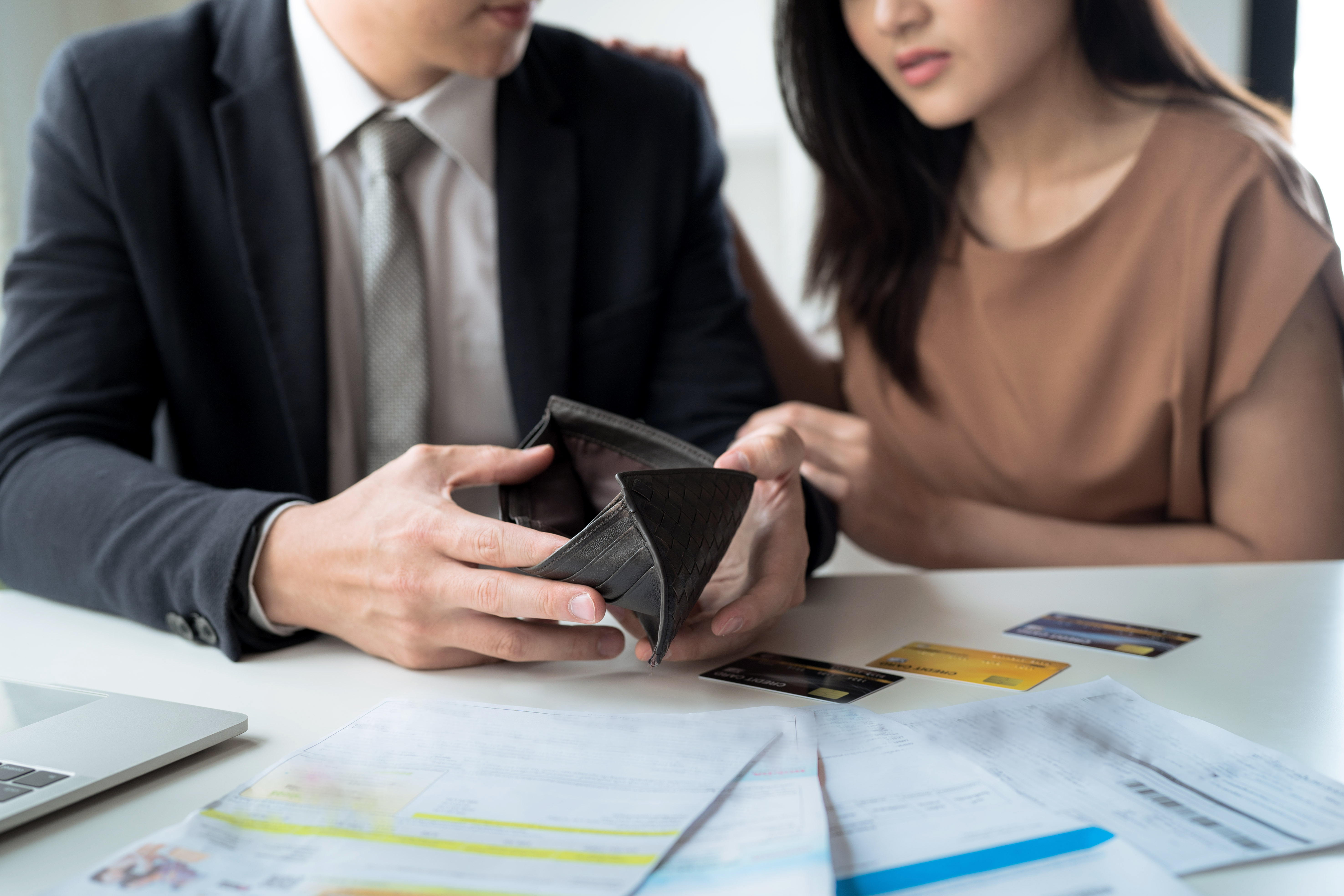 A man and women look into an empty wallet surrounded by credit cards and bills.