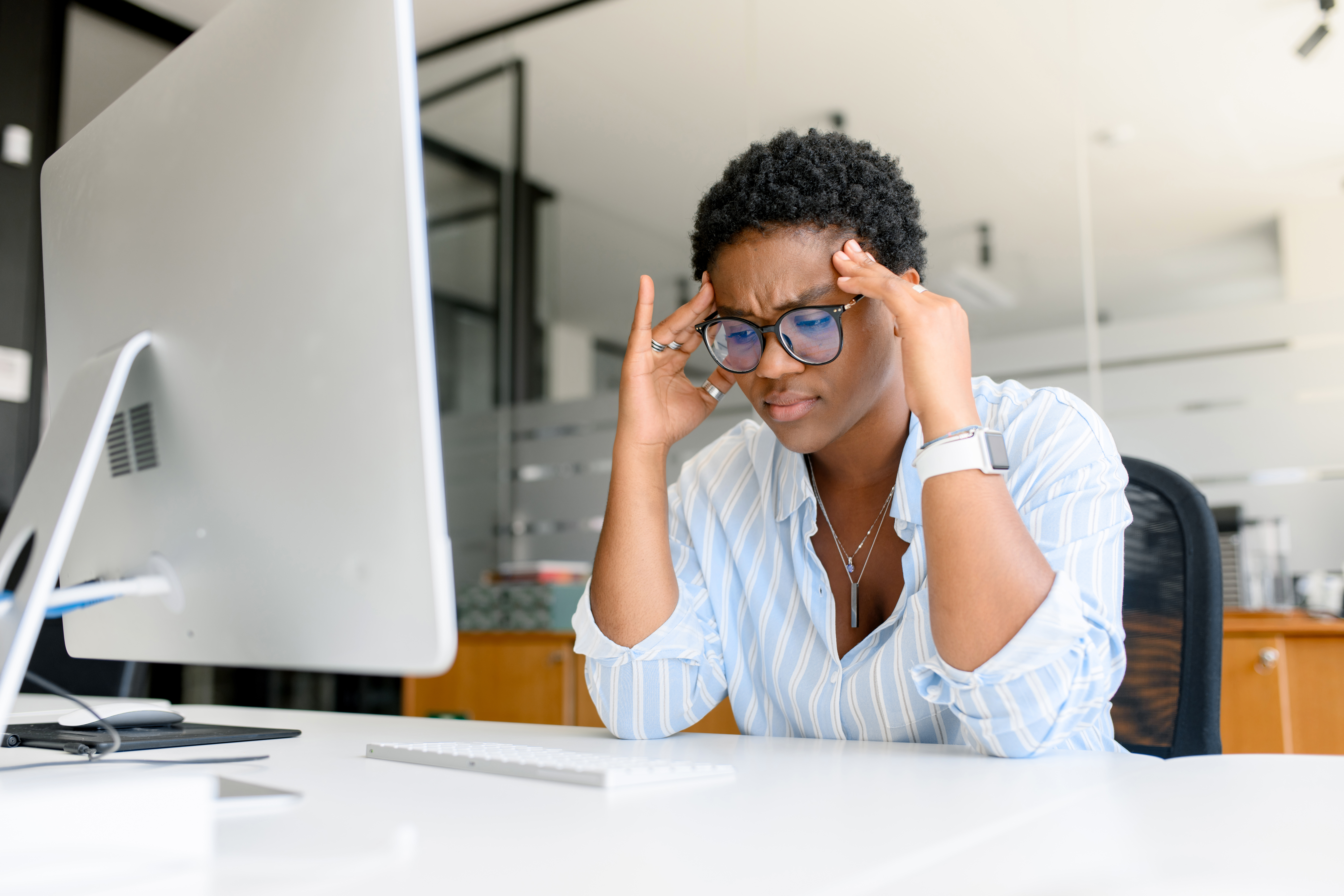 A woman looks upset and anxious looking at a large mac computer in an office